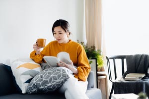 beautiful young asian woman reading a book while drinking a cup of coffee enjoying a quiet time and relaxing environment at cozy home