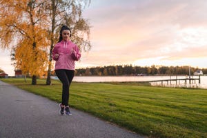 beautiful young female athlete jogging by a lake outdoors during a colorful sunset