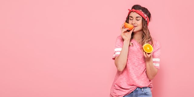 Beautiful young girl in pink t-shirt, keeps funny sexy orange on pink background. Summer and rest