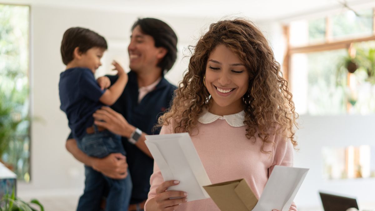 mother looking at the mail while dad and son play at background