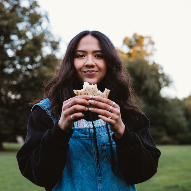 a beautiful young woman eating a sandwich in a public park
