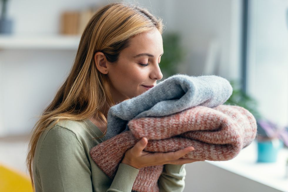 beautiful young woman holding and smelling clean clothes at home