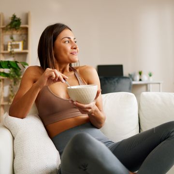 beautiful young woman is sitting on the sofa in the living room and eating oatmeal