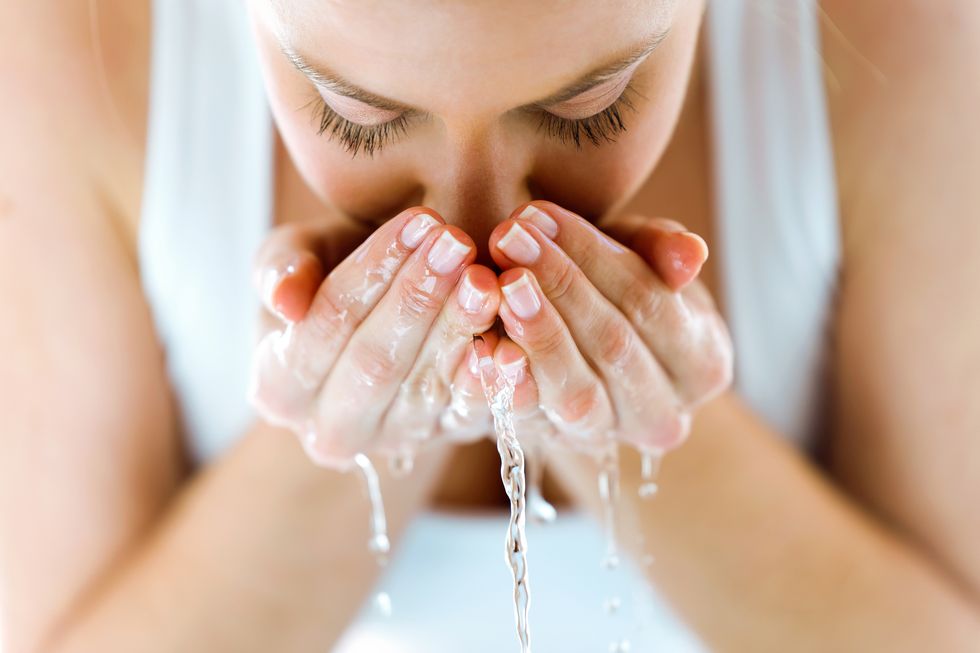 beautiful young woman washing her face splashing water in a home bathroom