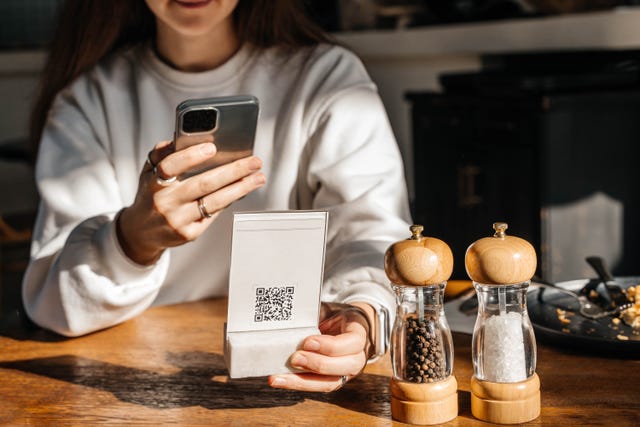 a beautiful young woman with long hair scans a qr code in a café to see the menu online