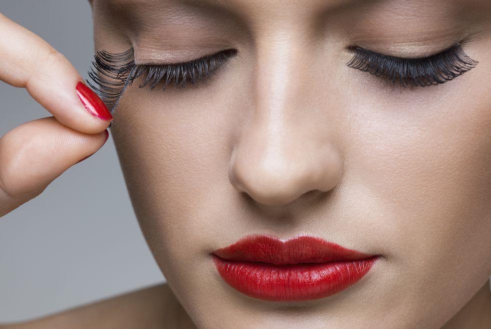 Beautiful young woman with red lipstick removing false eyelashes , studio shot