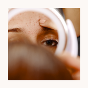 woman looking into a mirror touching an acne breakout on her forehead
