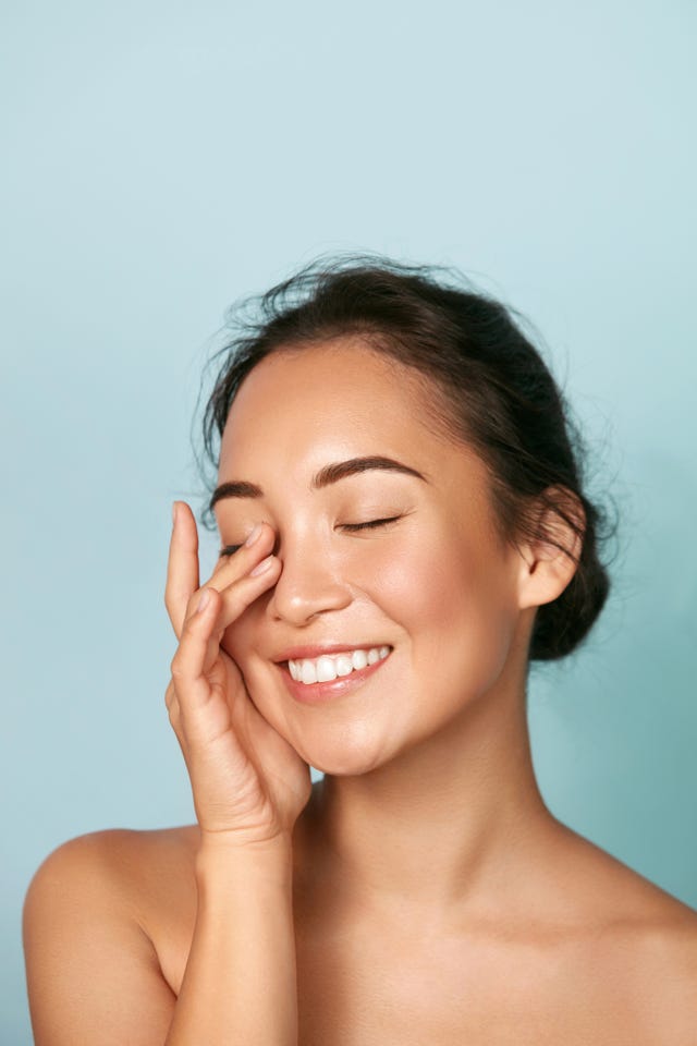 beauty face smiling asian woman touching healthy skin portrait beautiful happy girl model with fresh glowing hydrated facial skin and natural makeup on blue background at studio skin care concept