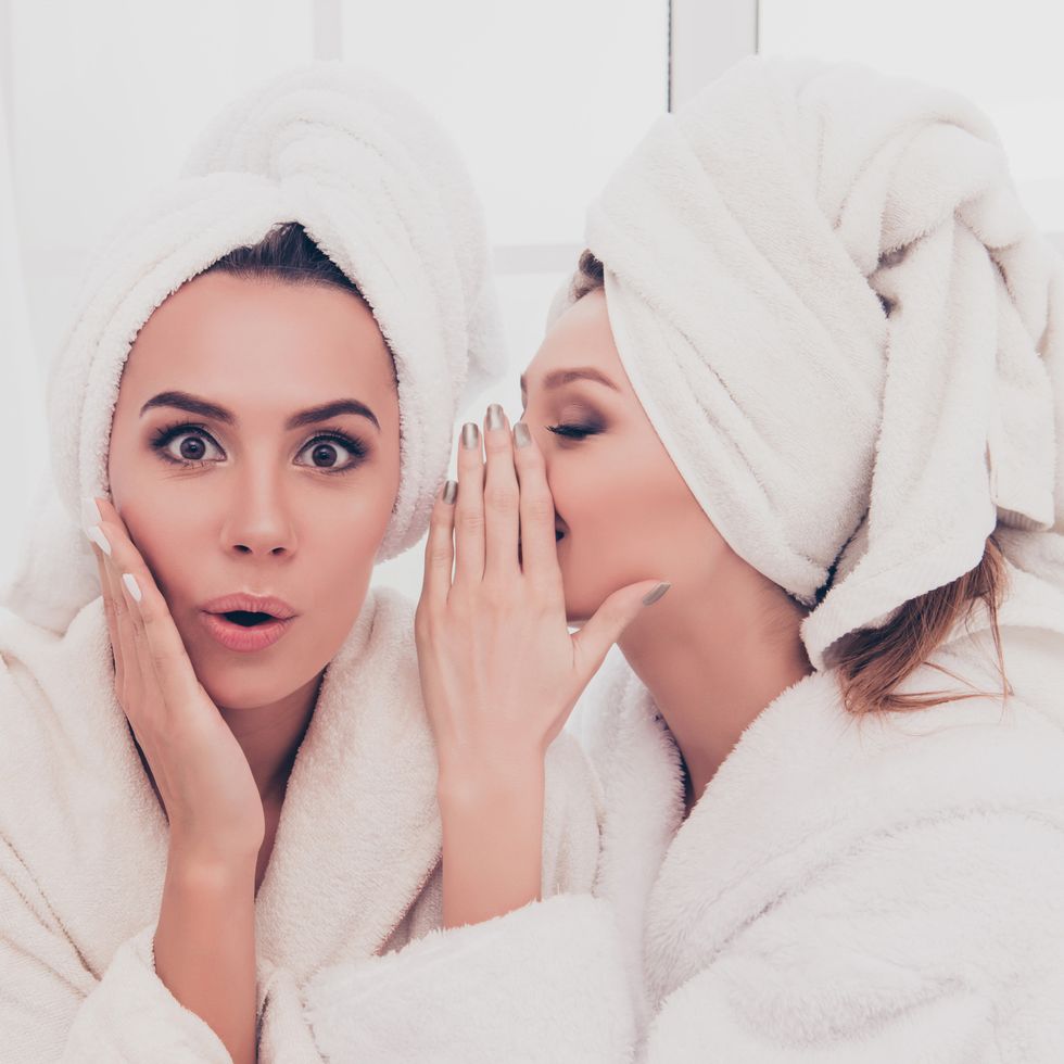 Portrait of young girl in bathrobe telling secret to her shocked sister