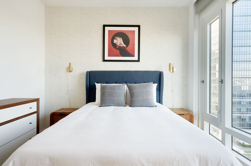 bedroom with a navy headboard, art of a girl, and gold sconces