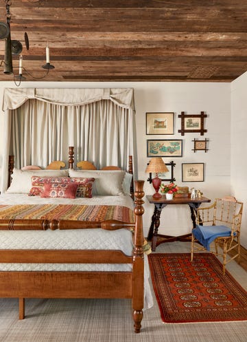 a classicly decorated farmhouse bedroom with wood furniture and a red rug and pretty linens and artwork