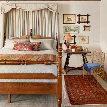 a classicly decorated farmhouse bedroom with wood furniture and a red rug and pretty linens and artwork