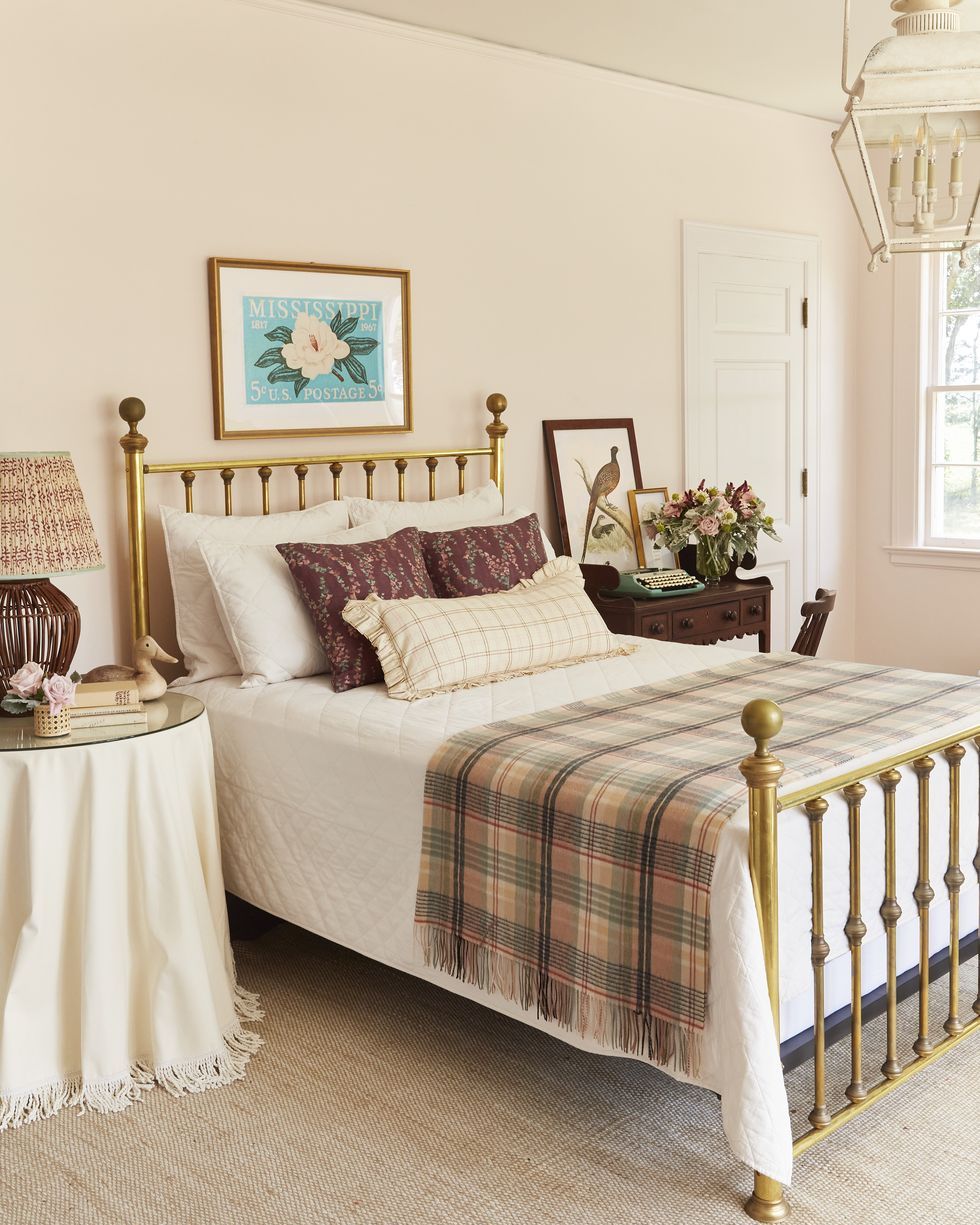 a light pink guest room with a brass bed and a plaid blanket