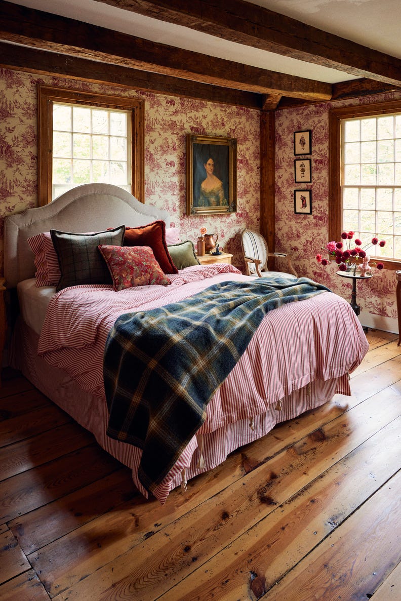 bedroom with red toile wallpaper and tan upholstered headboard with red striped bedding