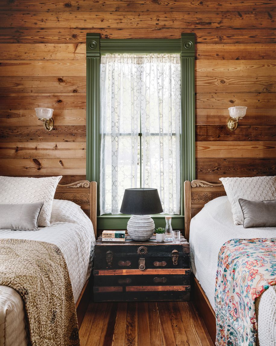 a bedroom in a1900s farmhouse in east texas that has pine walls and a green window trim and twin beds