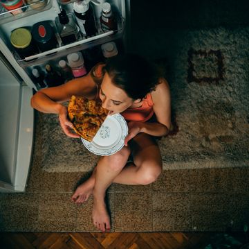 een vrouw eet in de avond een pizza uit de koelkast