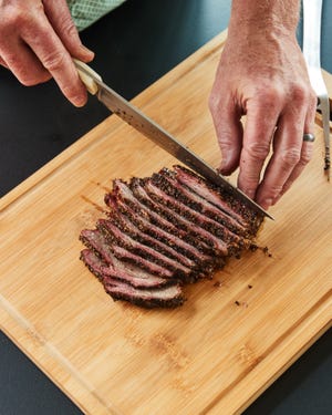 A person slicing a smoked brisket on a wooden cutting board