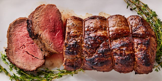 beef tenderloin sliced on a white platter served with rosemary