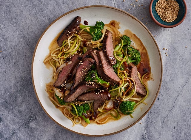 beef and broccoli stem "zoodles" with florets in a wide white bowl on a grey background