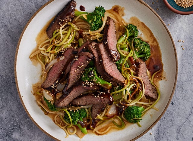 beef and broccoli stem "zoodles" with florets in a wide white bowl on a grey background beef and broccoli stem "zoodles" with florets in a wide white bowl on a grey background