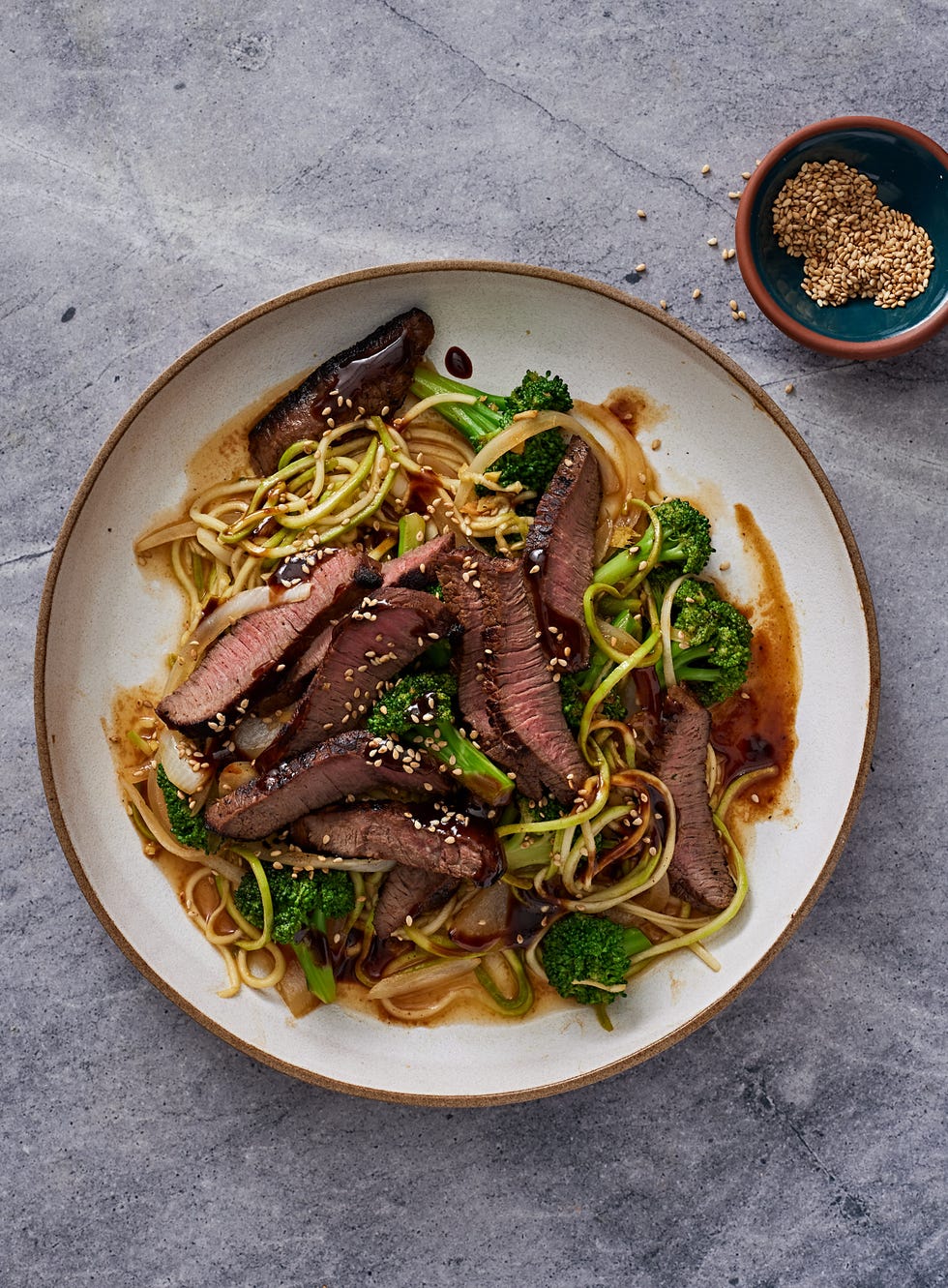 beef and broccoli stem "zoodles" with florets in a wide white bowl on a grey background