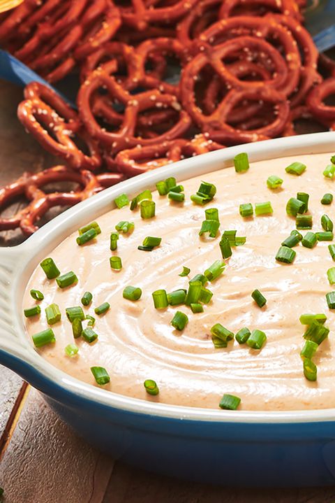 blue dish full of beer cheese dip garnished with scallions with pretzels in the background