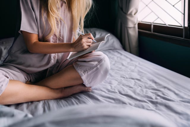 an unrecognizable caucasian female studying in the morning. she is sitting on the cozy bed in her bedroom.