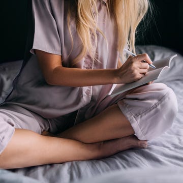 An Unrecognizable Beautiful Blonde Woman In Pajamas Writing Her Diary an unrecognizable caucasian female studying in the morning. she is sitting on the cozy bed in her bedroom.
