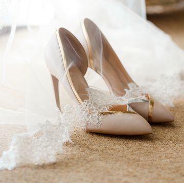 beige bridal shoes standing on the floor, covered with a white veil with lace a pair of expensive and beautiful wedding shoes with high heels, with gold and silver finish