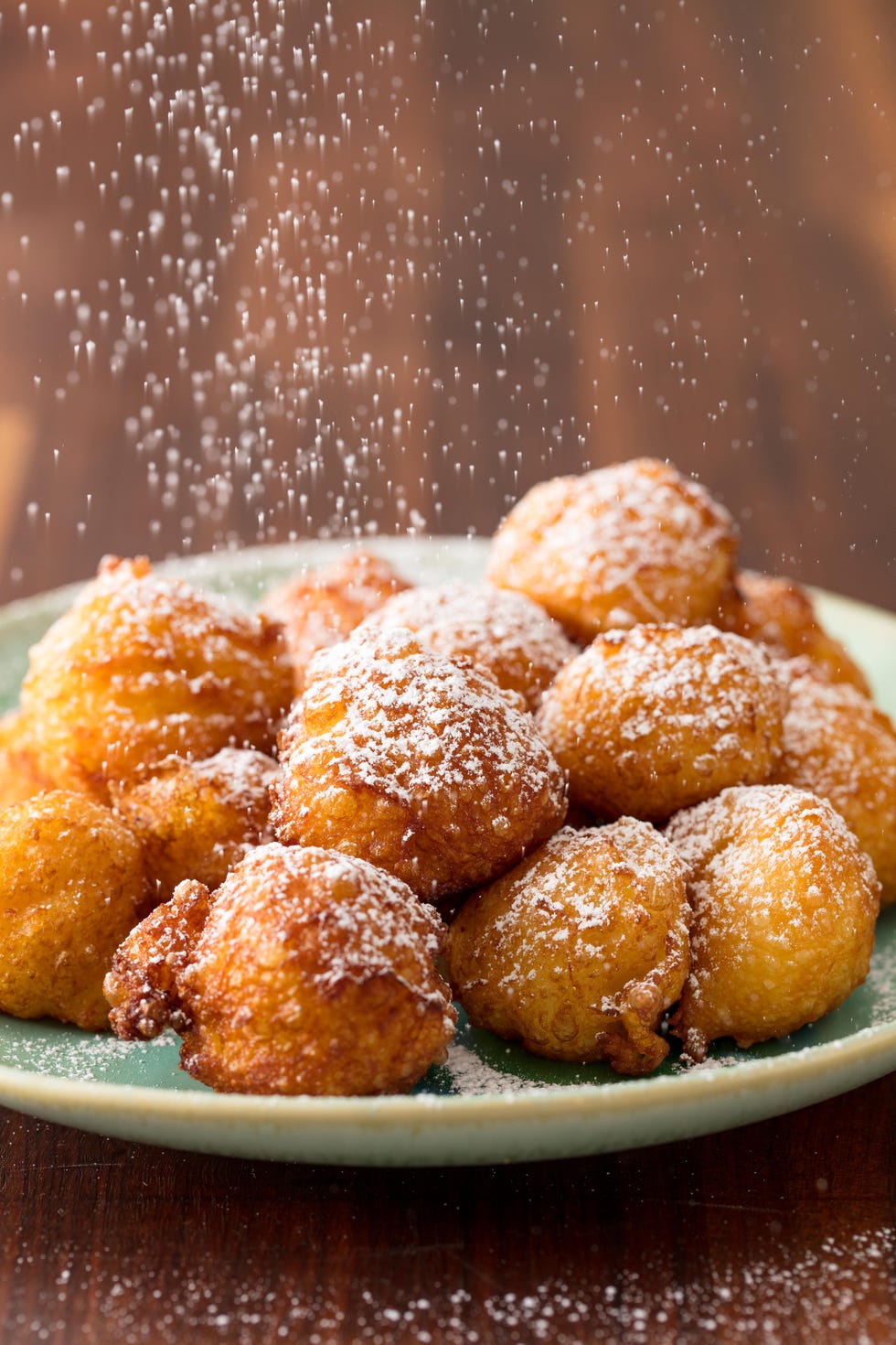 beignets on a plate being sprinkled with powdered sugar