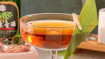 cocktail in a coupe glass with a bamboo leaf garnish