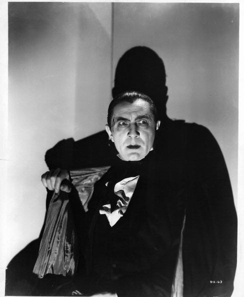 bela lugosi portraying dracula, wearing a black suit and standing in the shadows