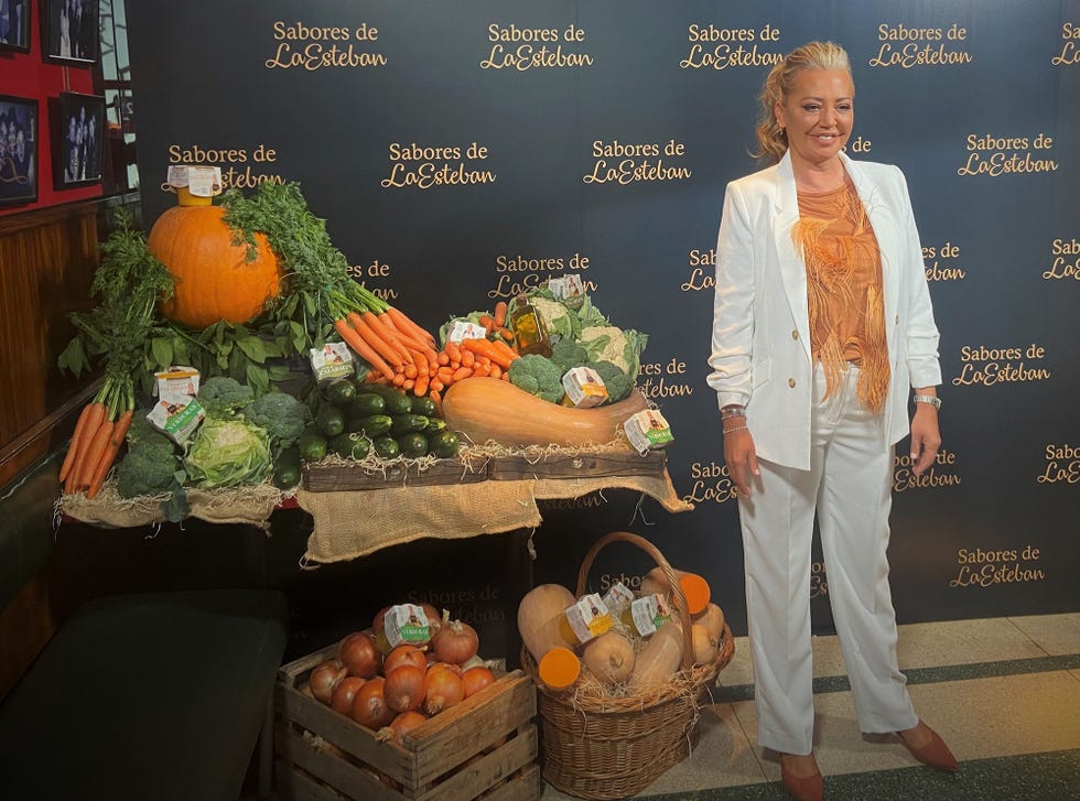 la colaboradora con un traje blanco junto a sus nuevos productos y un bodegón de verduras