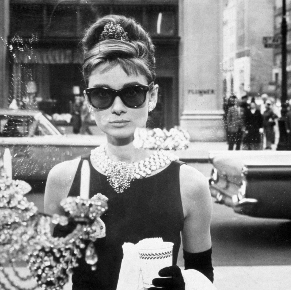1961 belgianborn actor audrey hepburn 1929 1993, as holly golightly, holds a cup and a paper bag while looking into one of the window displays at tiffany's in a still from the film, 'breakfast at tiffany's,' directed by blake edwards she wears sunglasses, a little black dress, long gloves and a tiara in her chignon photo by paramount picturesgetty images
