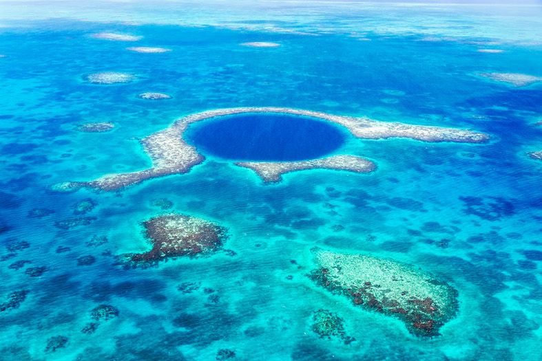 beautiful azure blues surround the dark navy coloured sink hole in the caribbean sea surrounding belize