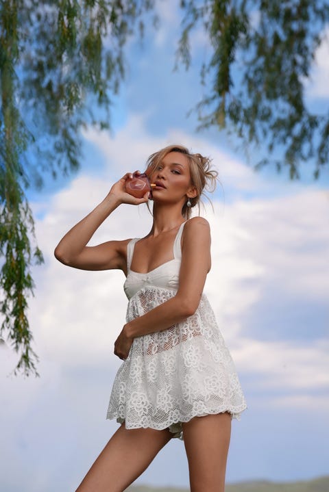 a woman in a white lace dress holding a drink outdoors