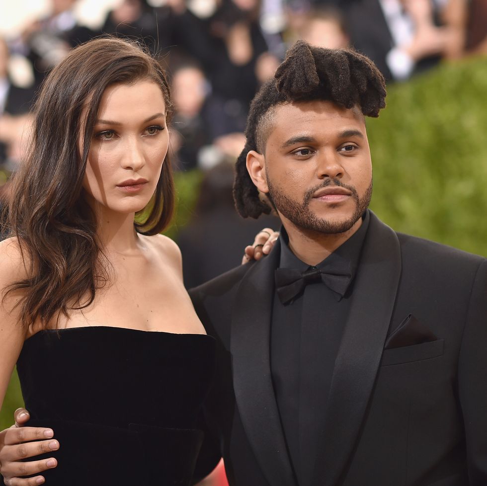 a woman in a black strapless dress and a man in an all black tuxedo embrace as they pose for photos and look to the right
