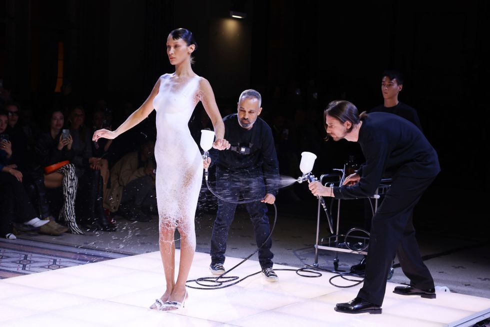 model being spray painted into a white dress by two men in black clothing