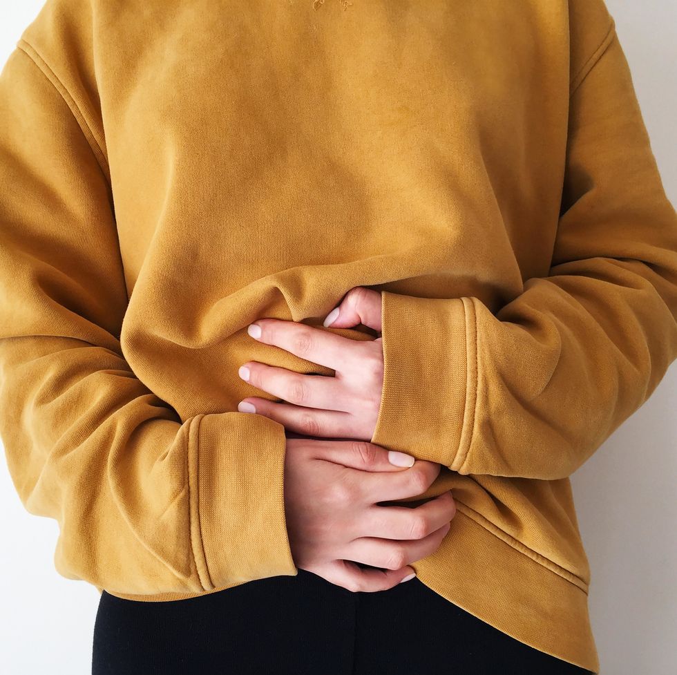 woman wearing a sweatshirt with both hands touching her abdomen