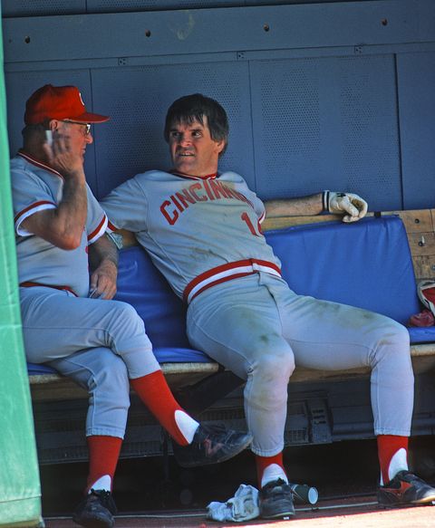 pete rose sitting in a dugout talking to one of his coaches