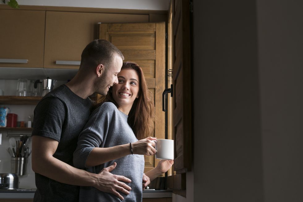 Amorous couple standing in kitchen, embracing with cup of coffee