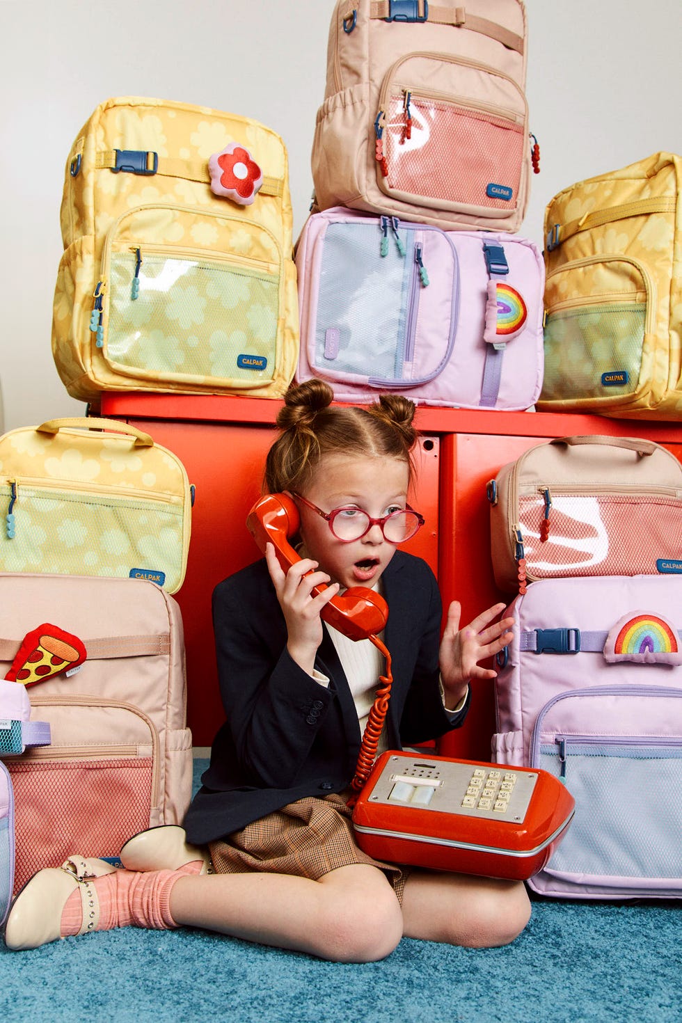 child using a vintage telephone surrounded by colorful backpacks