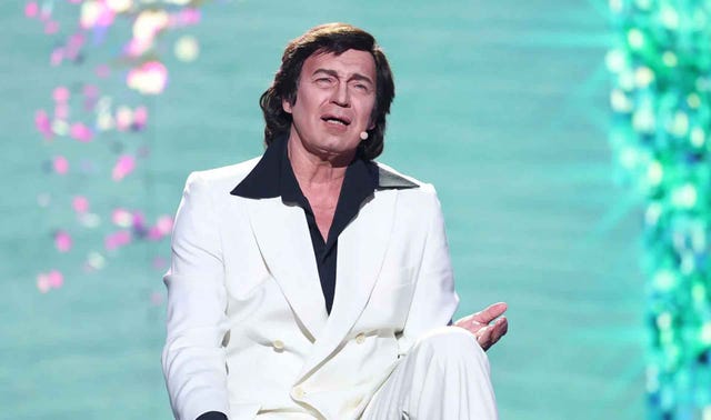 a person in a white suit seated with a confident posture