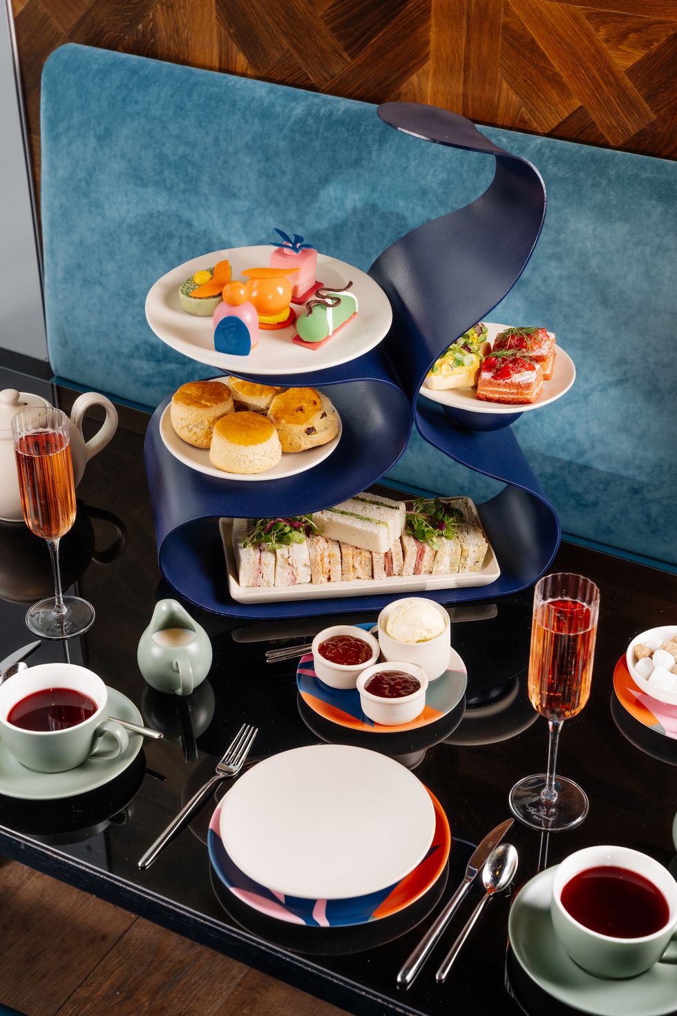 a table with afternoon tea piled prettily onto a blue stand, with cakes, scones and sandwiches, surrounded by flutes and tea