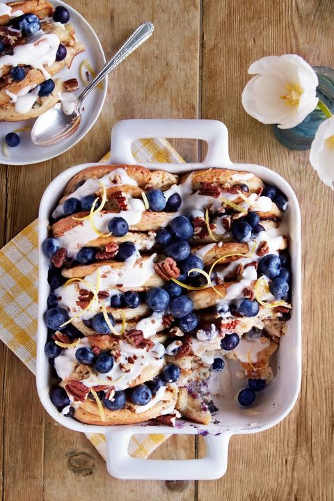 blueberry pecan pancake bread pudding in a white square casserole dish topped with honey sour cream sauce and lemon zest