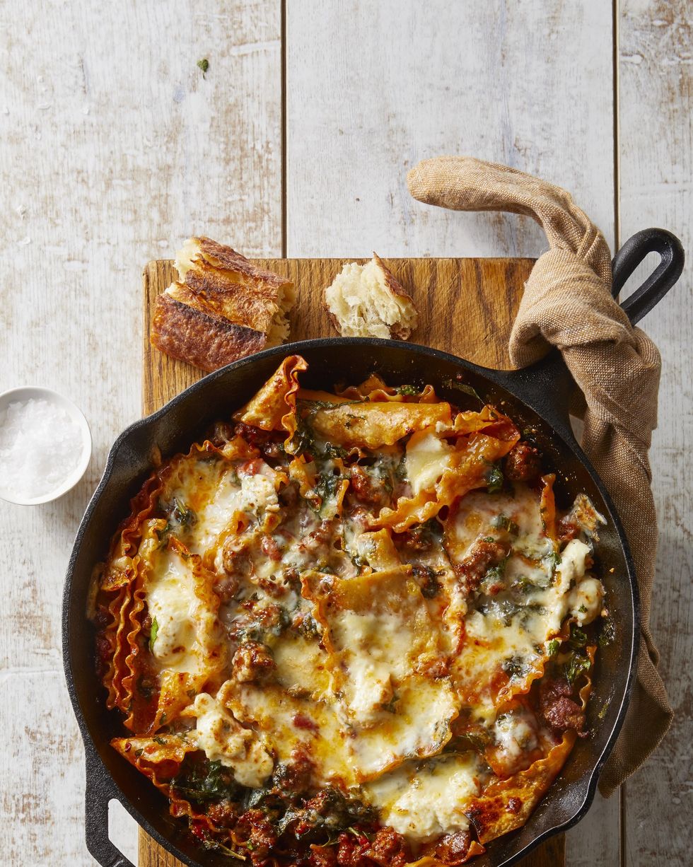 sausage and cheese lasagna in a cast iron skillet on a wooden cutting board