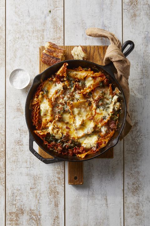 sausage and cheese lasagna in a cast iron skillet on a wooden cutting board