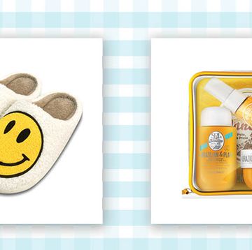 a pair of sherpa cream colored slip on slippers with smiley faces on them and a yellow and clear bag filled with lotion, body wash and body spray