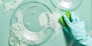 best cleaning tips a person with a rubber glove on uses a sponge to clean dishes and the kitchen countertop