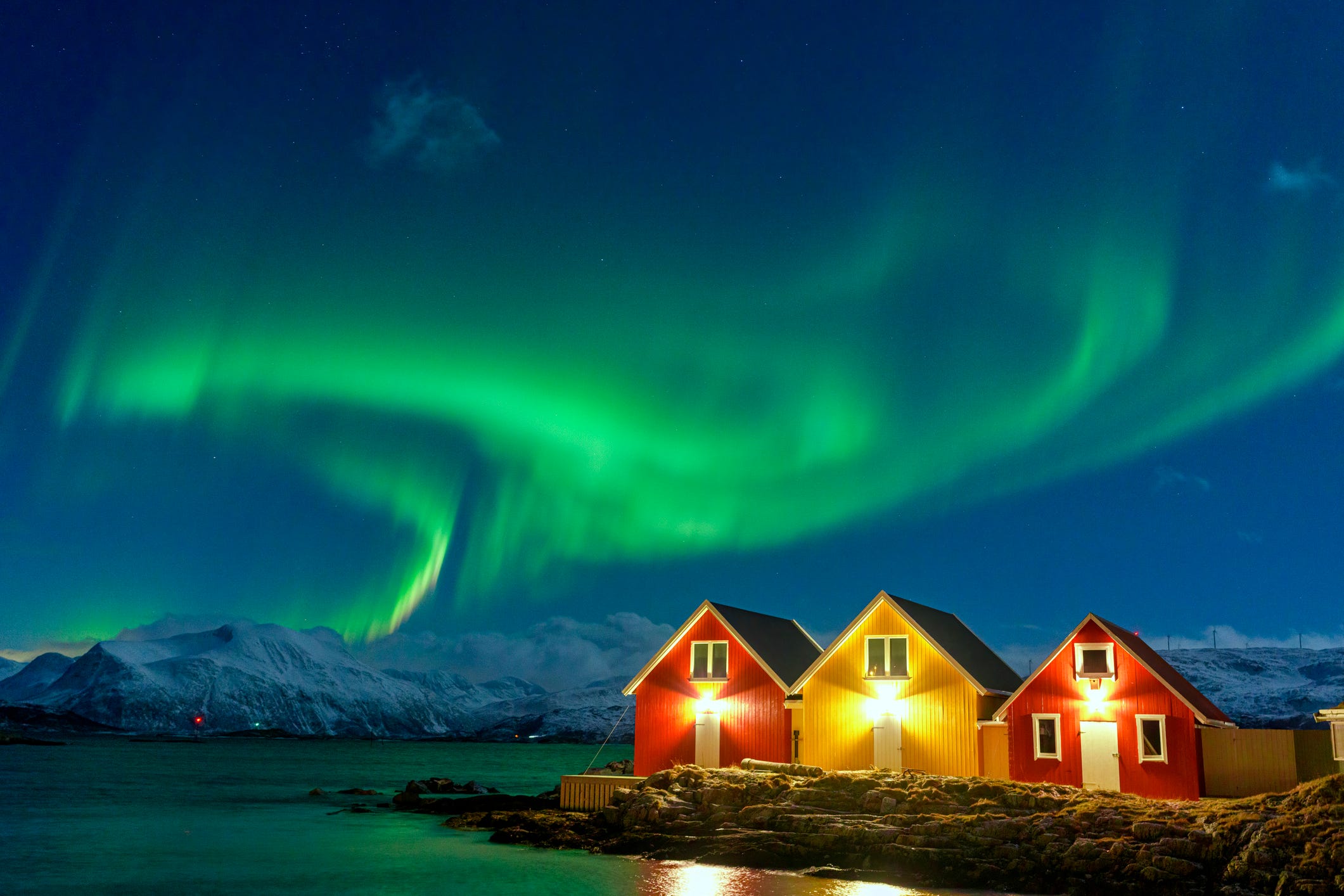 aurora borealis over snowcapped mountains and fishermen cabins by the sea, sommaroy, troms og finnmark, norway